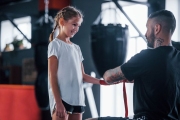 Helping to wear the bandages. Young tattooed boxing coach teaches cute little girl in the gym